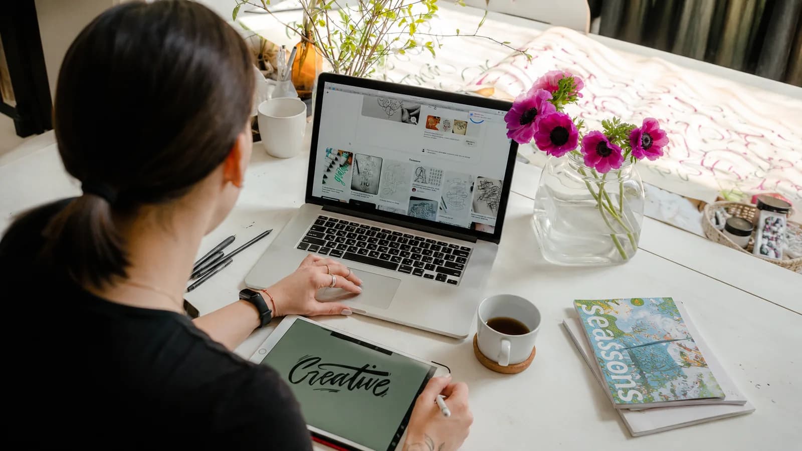 A creative professional working across a laptop and tablet at a bright desk